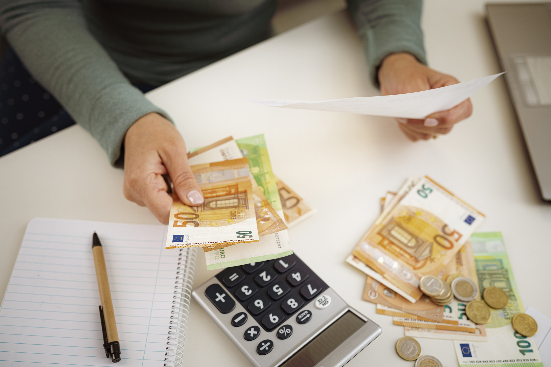 Manos contando billetes de euro junto a una calculadora sobre una mesa