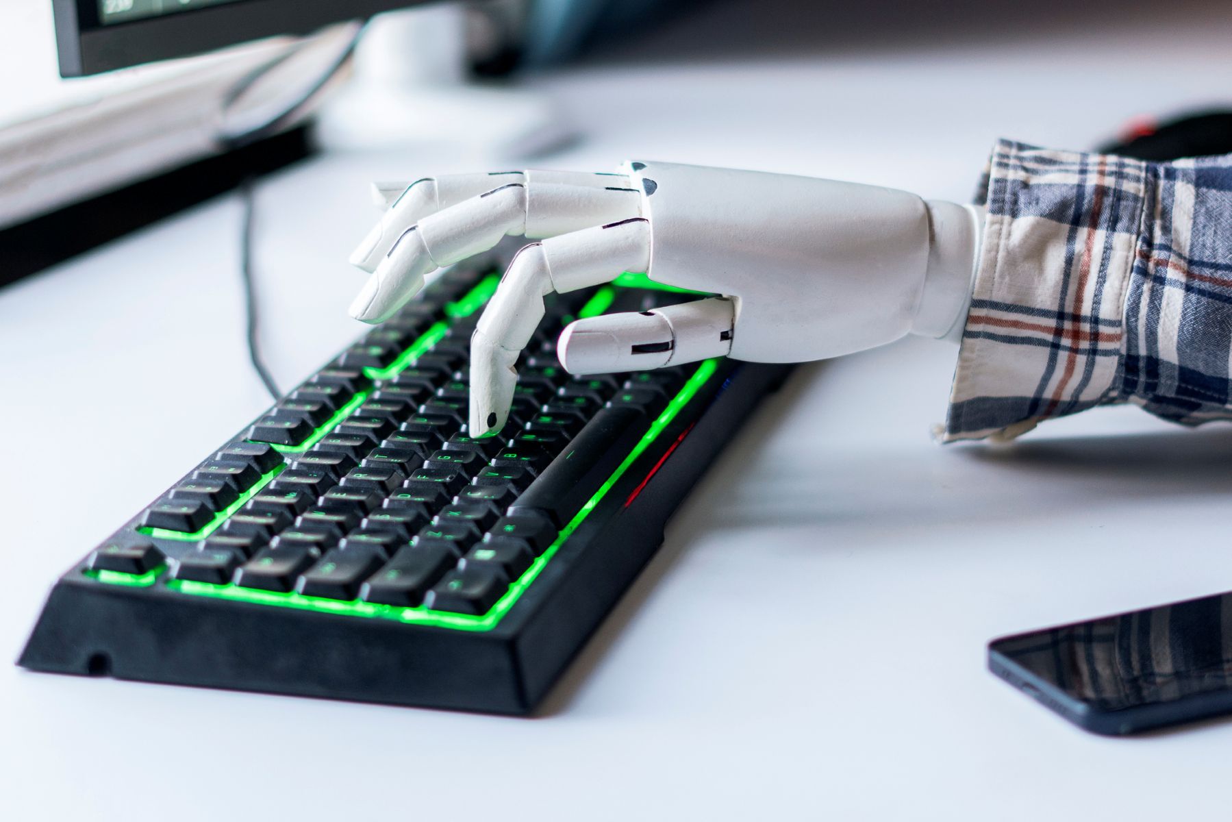 Brazo de robot vestido con camisa, con el índice de la mano pulsando un teclado de ordenador sobre una mesa de escritorio